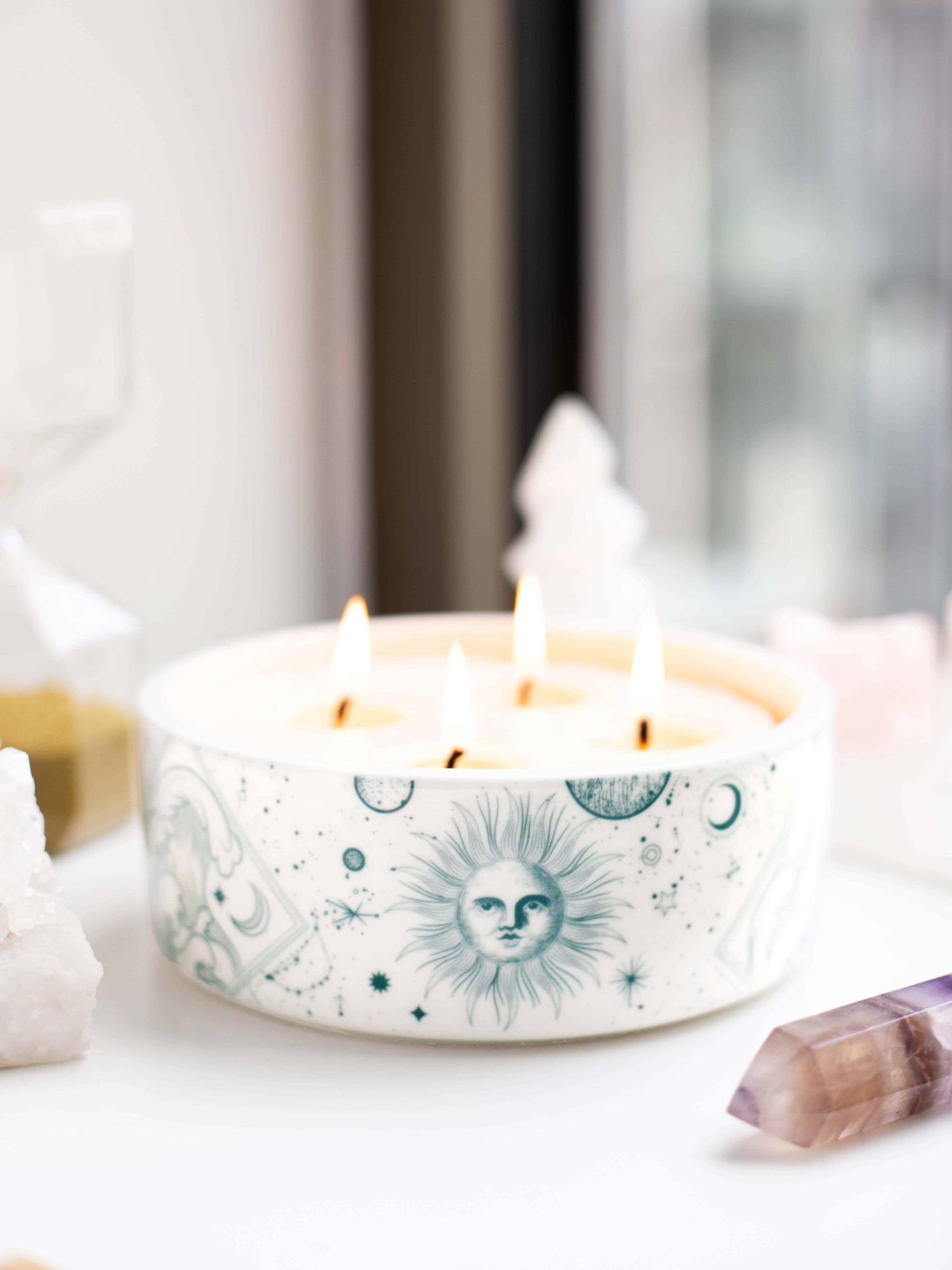 four wick candle with a ceramic vessel design of whimsical constellations, stars, planets and the sun in the middle